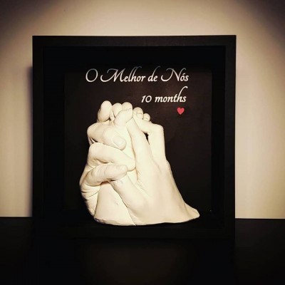 Escultura de mãos dadas com texto 'O Melhor de Nós 10 months' em moldura preta
