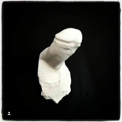 Escultura branca em formato fálico sobre fundo preto