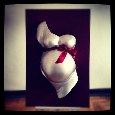 Busto de gravidez com fita vermelha numa placa preta