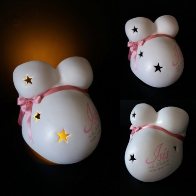 Molde branco de barriga de gravidez com estrelas recortadas e fita rosa num fundo preto.