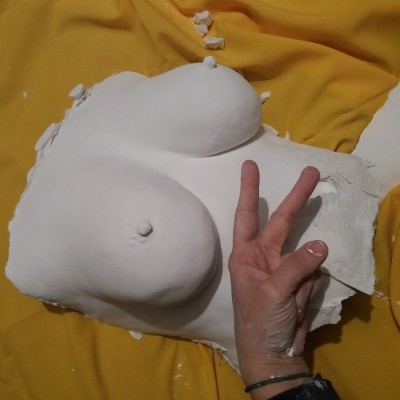 Molde de gesso branco do torso feminino sobre tecido amarelo com mão visível