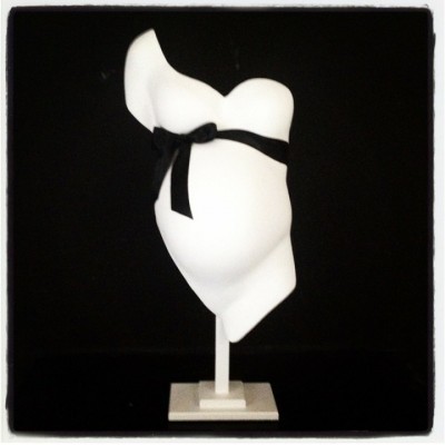 Escultura branca de torso de grávida com fita preta no peito, em pedestal branco