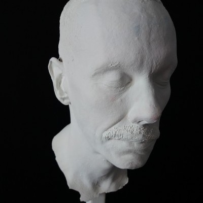 Escultura branca de cabeça humana com bigode e olhos fechados