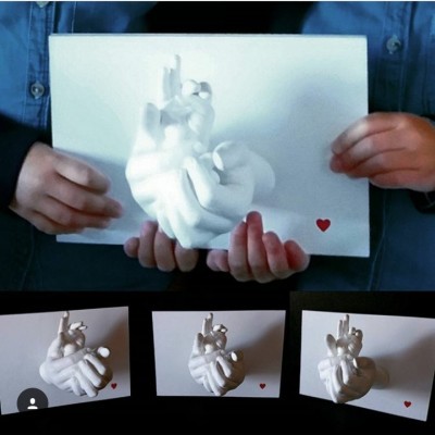 Caixa branca com escultura de mão branca e coração vermelho