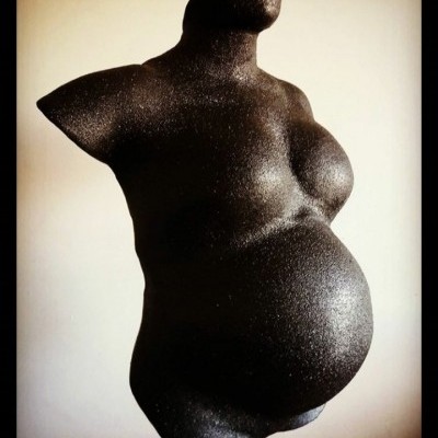 Escultura preta rugosa de torso feminino grávido sem cabeça nem membros