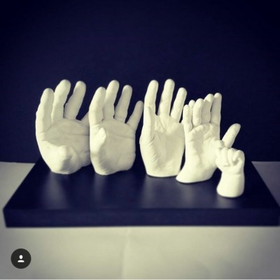 Esculturas brancas de mãos humanas de vários tamanhos numa base preta