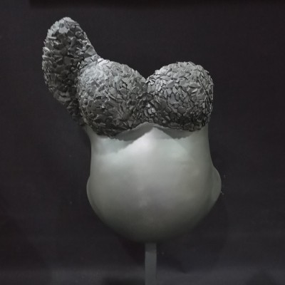 Escultura cinzenta de torso feminino com top texturizado sobre fundo preto