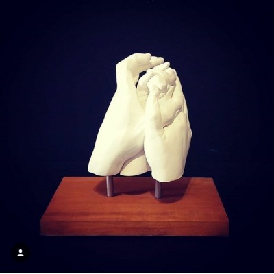 Escultura branca de duas mãos entrelaçadas sobre base de madeira