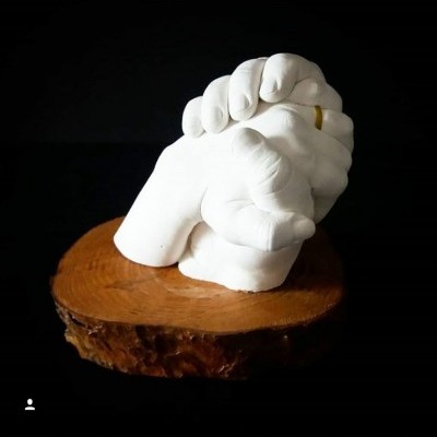 Escultura em gesso de mãos entrelaçadas com anel dourado sobre base de madeira