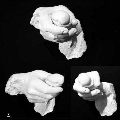 Escultura branca de mão segurando uma esfera sobre fundo preto.