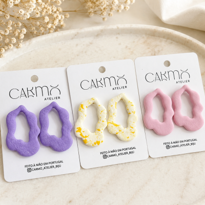 Três pares de brincos coloridos em cartão branco sobre prato claro
