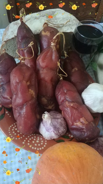 Salames curados vermelhos com alho, pão, vinho tinto e abóbora numa mesa