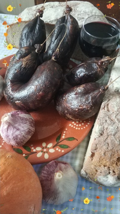 Prato com enchidos pretos, alho, pão e copo de vinho tinto sobre toalha xadrez