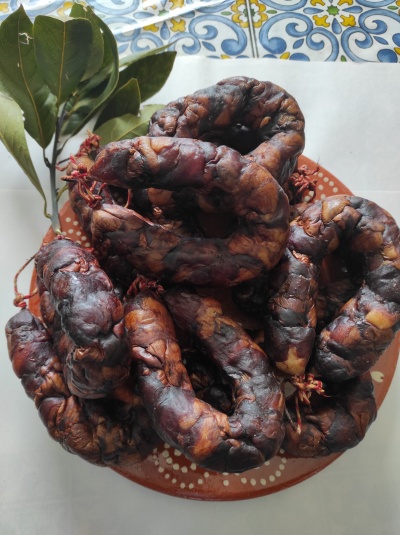 Salsichas tradicionais escuras num prato de barro com folhas verdes ao lado