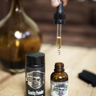 Frasco com óleo de barbear e embalagem preta de pó modelador sobre madeira