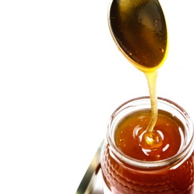 Frasco de vidro com mel dourado e colher a despejar mel.