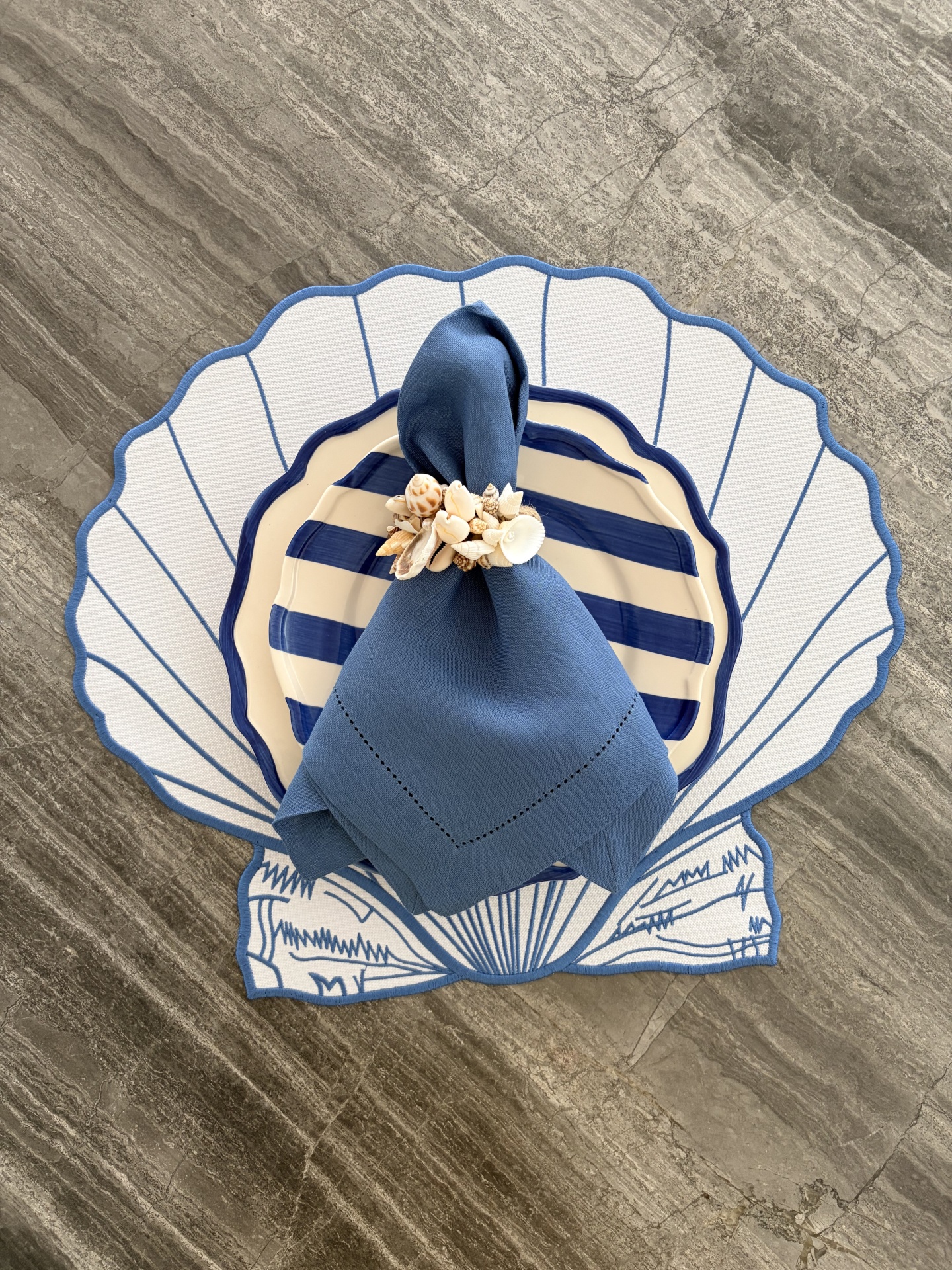 Conjunto de pratos com guardanapo azul e suporte em formato de concha em superfície cinza