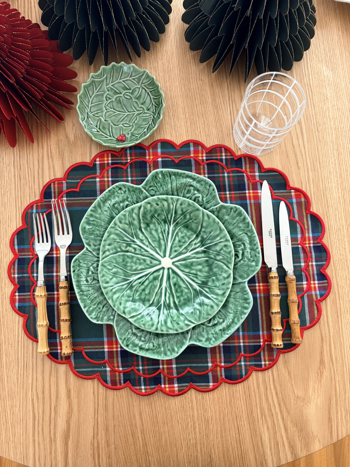 Conjunto de mesa com pratos verdes em forma de folha, talheres com cabo em bambu, toalhetes xadrez e copo transparente.