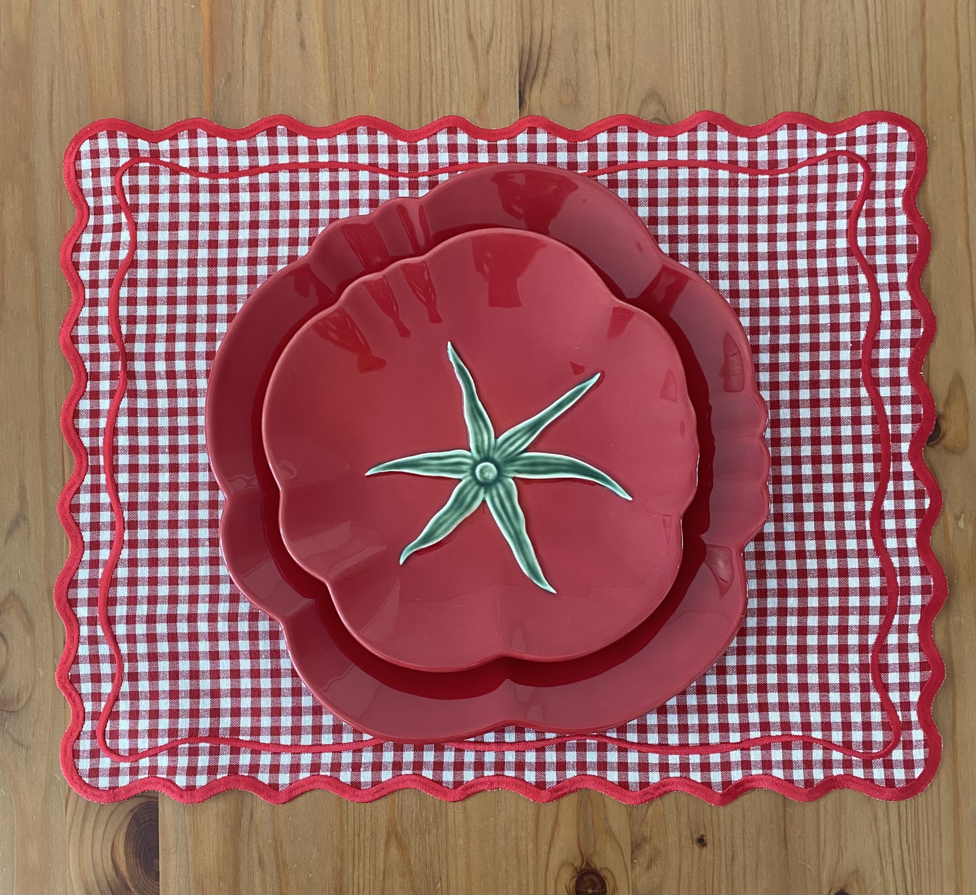 Dois pratos vermelhos em forma de tomate sobre jogo americano vermelho e branco, em mesa de madeira