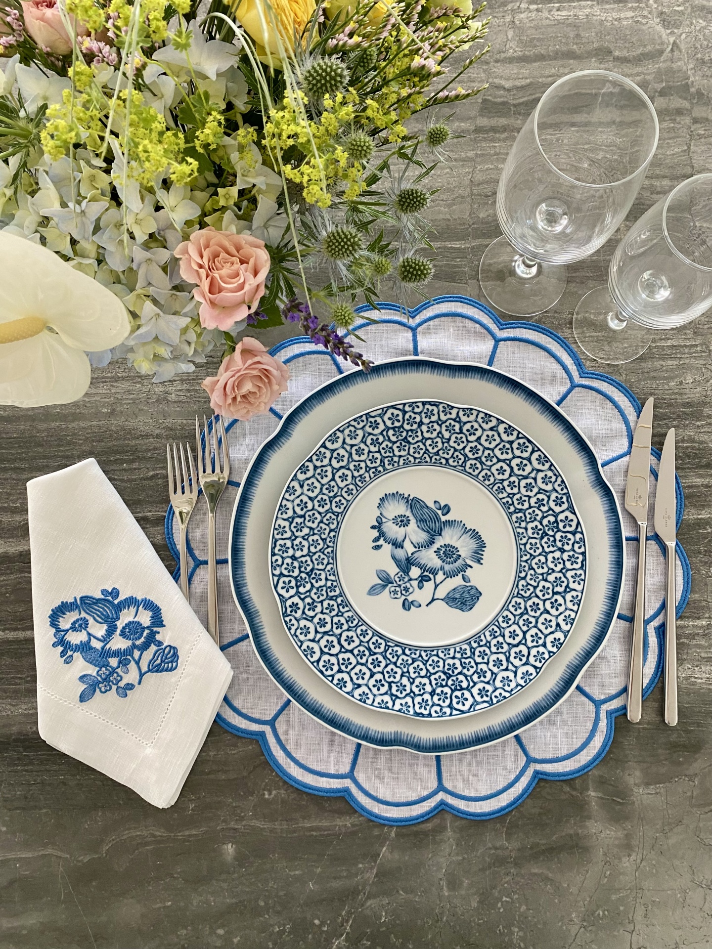 Mesa posta com prato azul e branco, guardanapo bordado, talheres e flores
