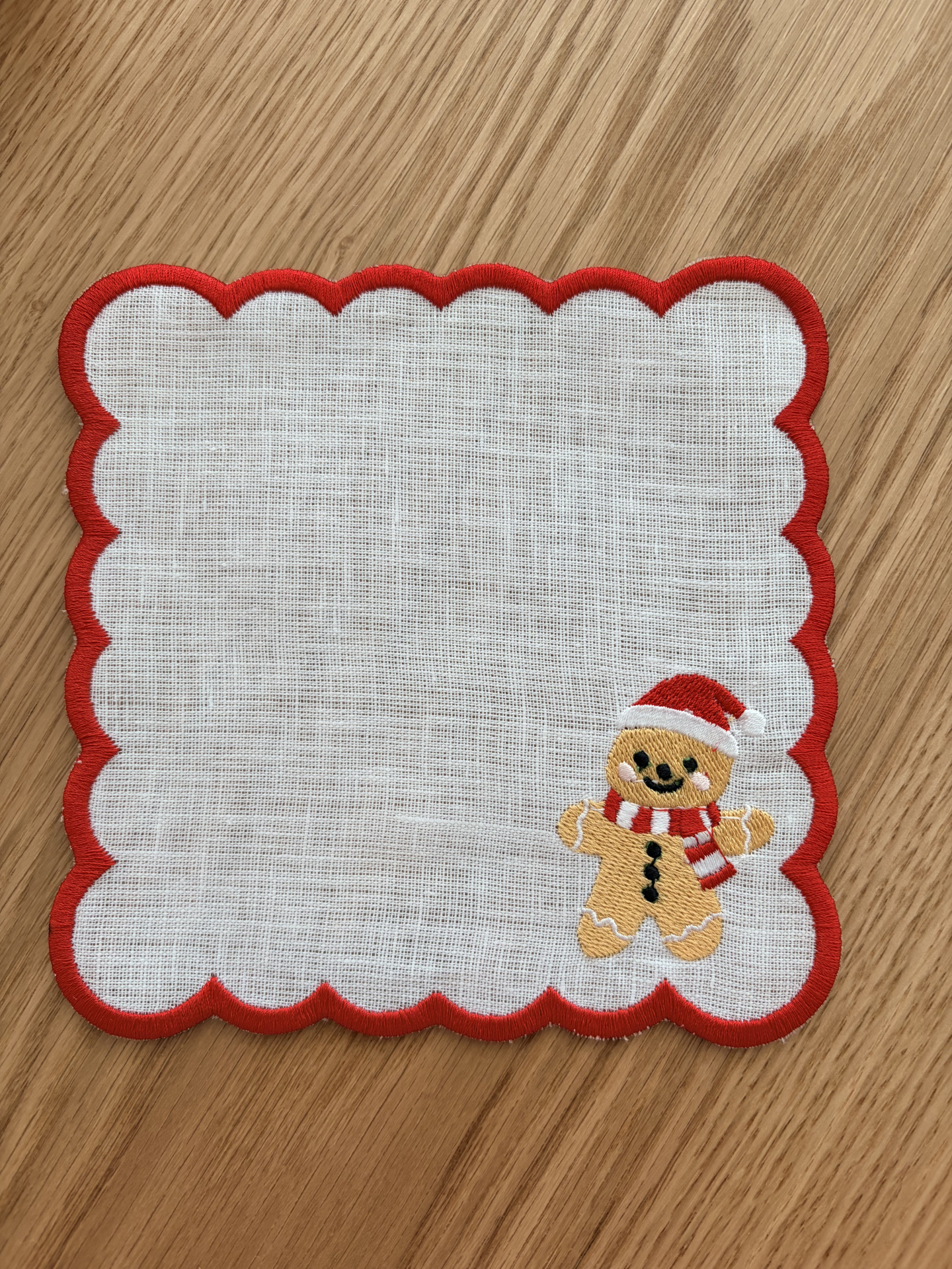 Toalhete branco com borda vermelha e boneco de gengibre bordado.