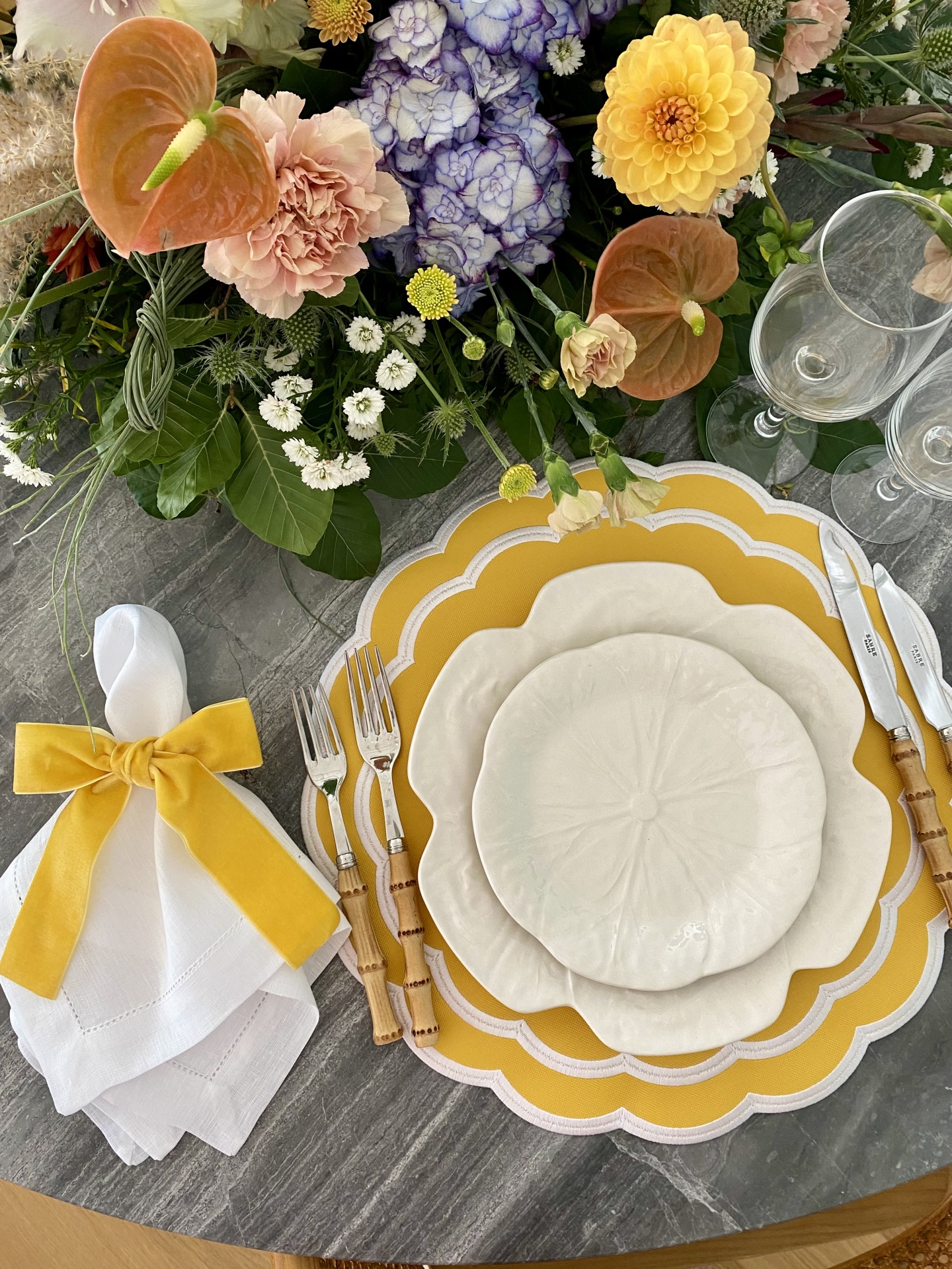 Conjunto de loiça branca com pratos amarelos, talheres de cabo madeira, guardanapo com laço amarelo e flores coloridas