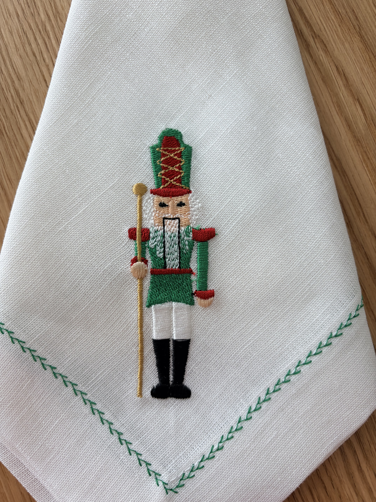 Guardanapo branco com bordado de soldado de brinquedo colorido e borda verde em padrão de folhas.