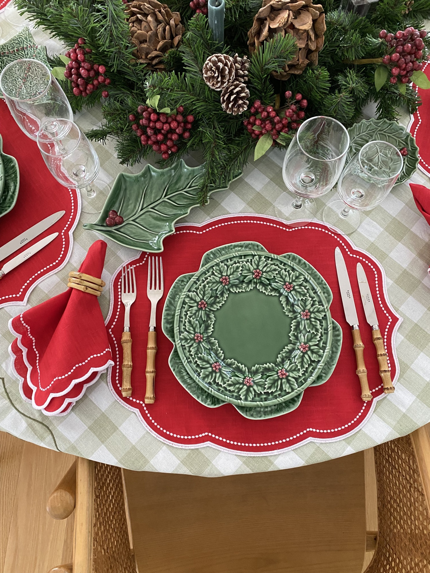 Conjunto de loiça de cerâmica verde com padrão de folhas e bagas vermelhas numa mesa com individual vermelho, talheres de cabo de madeira e guardanapo vermelho