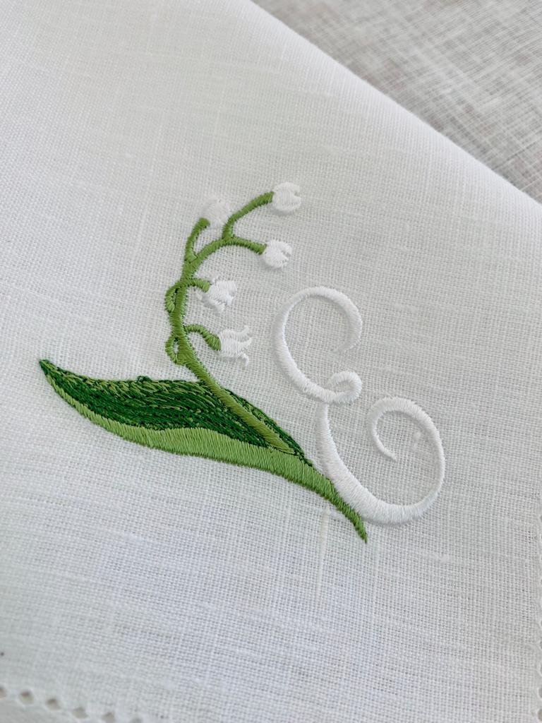 Pano branco com bordado de ramo verde com flores brancas e letra E em branco