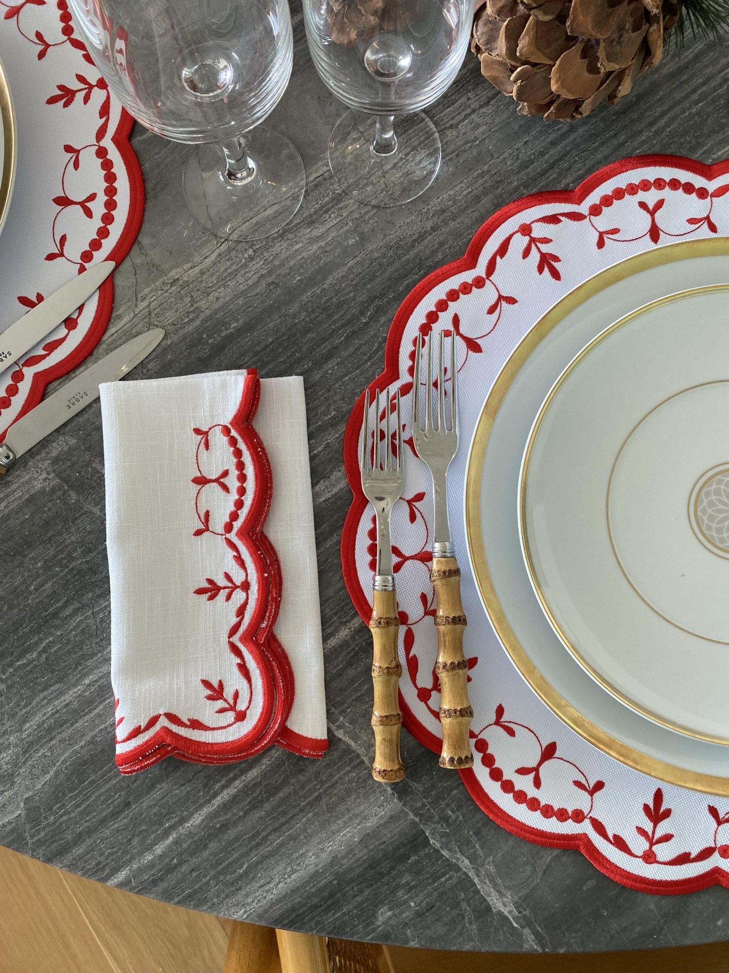 Conjunto de jantar com guardanapo bordado vermelho, pratos brancos com dourado e talheres com cabos de madeira