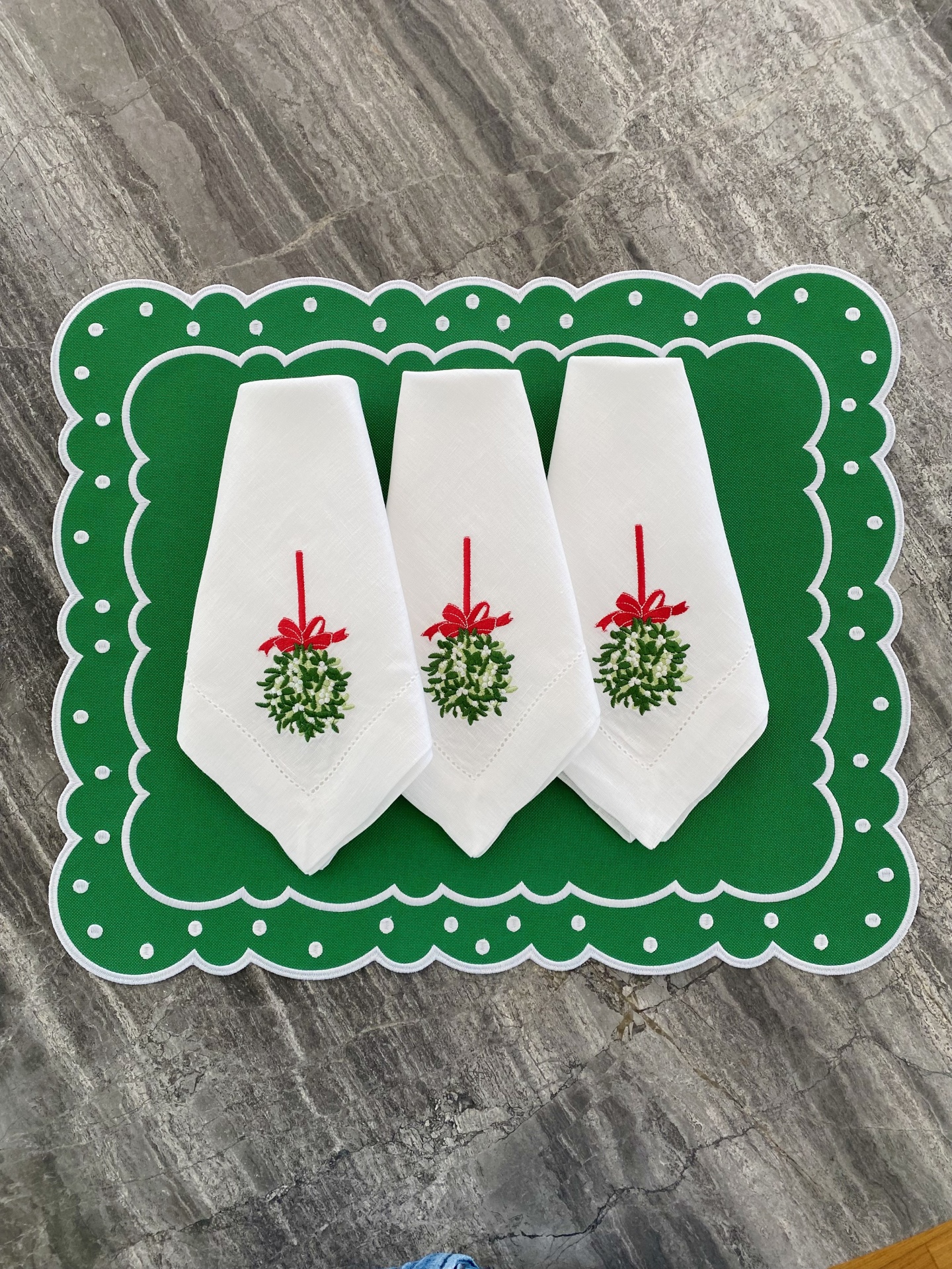 Três guardanapos brancos bordados com ramo verde e fita vermelha sobre tapete verde com pontos brancos