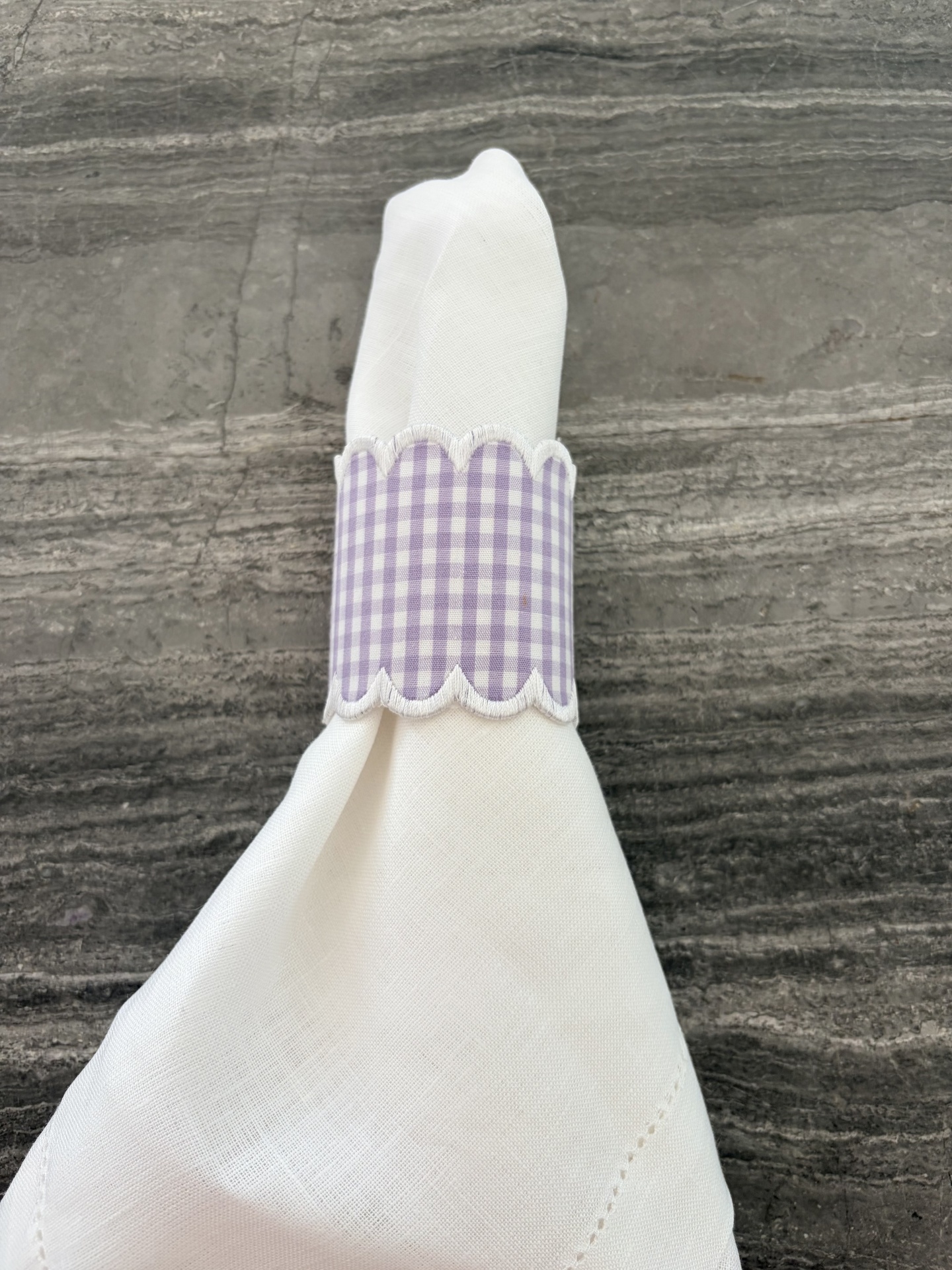 Guardanapo branco com argola lilás xadrez sobre mesa cinzenta