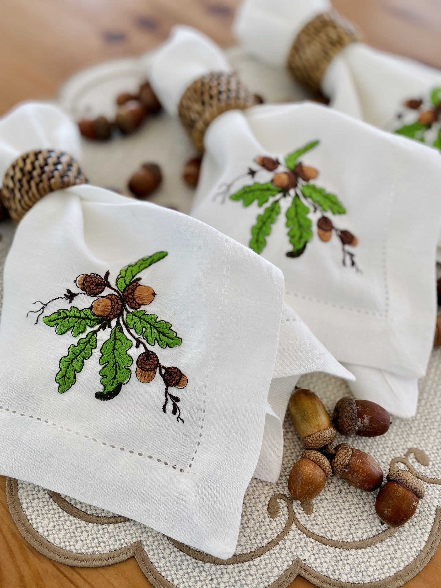 Guardanapos bordados com ramos de carvalho e bolotas com argolas trançadas sobre suporte decorativo