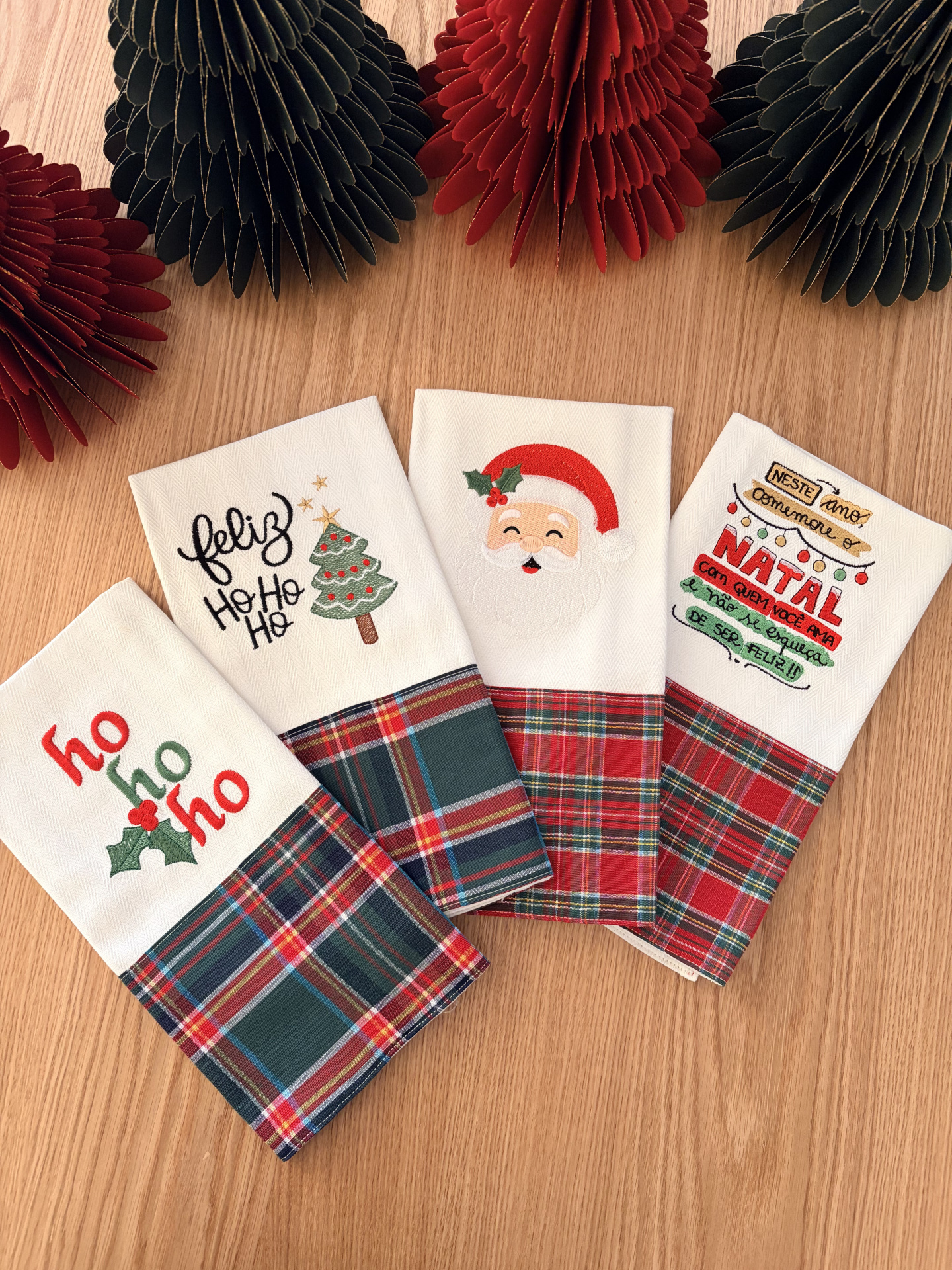 Toalhas de Natal com bordados e padrão xadrez sobre mesa de madeira clara