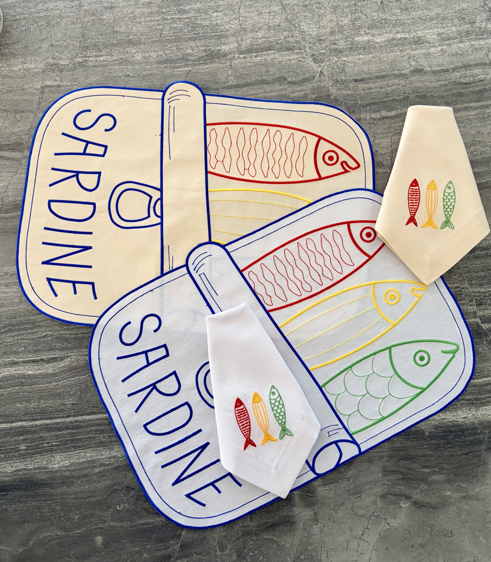 Utensílios de cozinha em tecido com estampas de peixes coloridos sobre superfície cinzenta