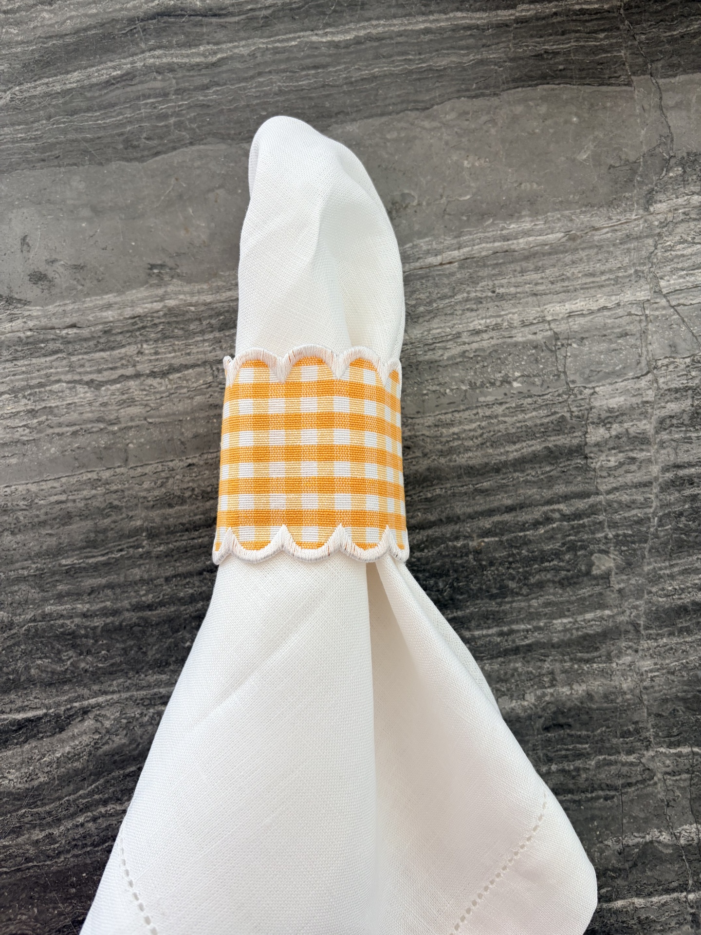 Guardanapo branco com argola xadrez amarelo e branco numa superfície cinza escura