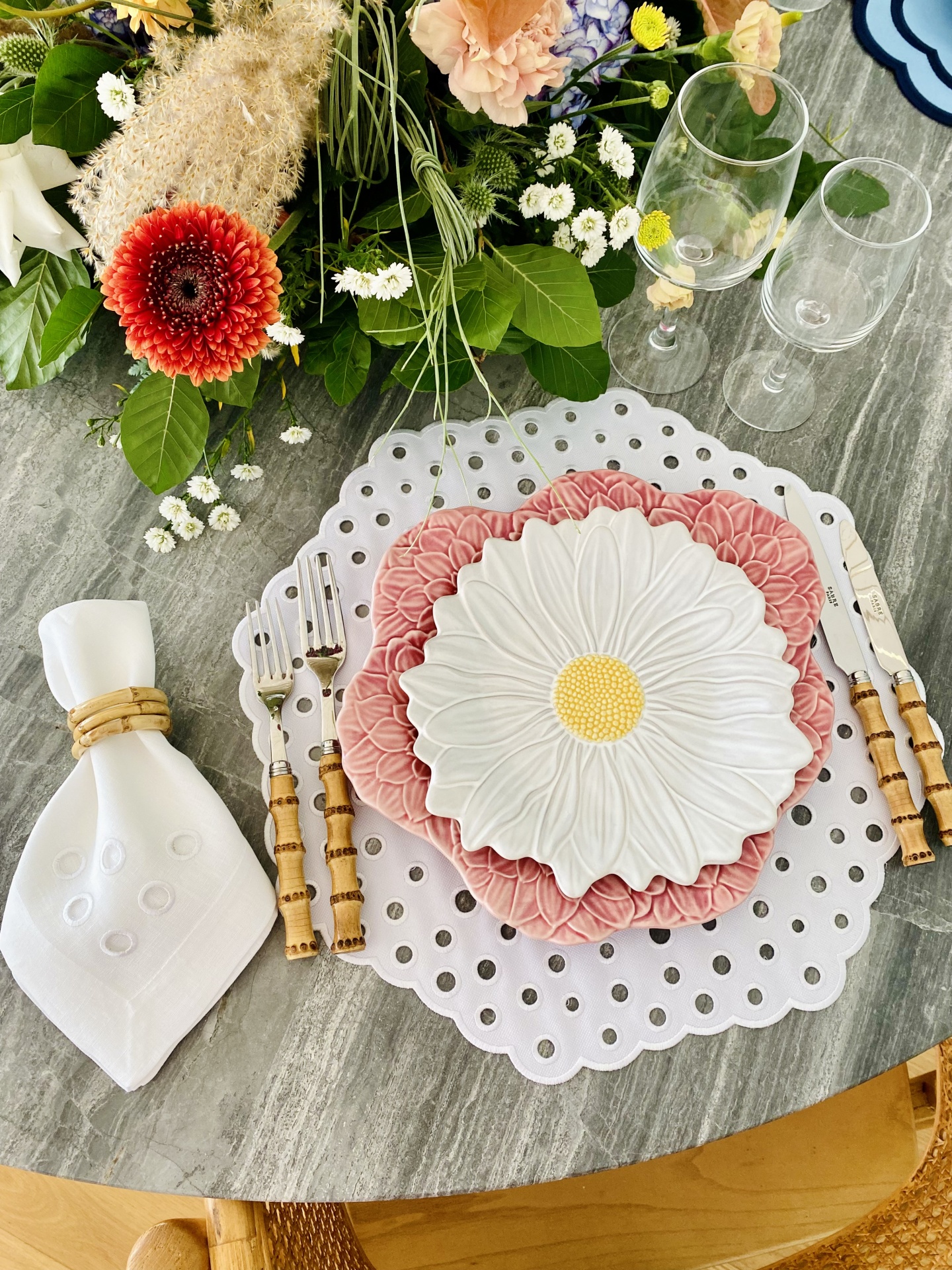 Mesa posta com pratos em forma de flor, talheres com cabo de madeira, guardanapo branco e flores coloridas