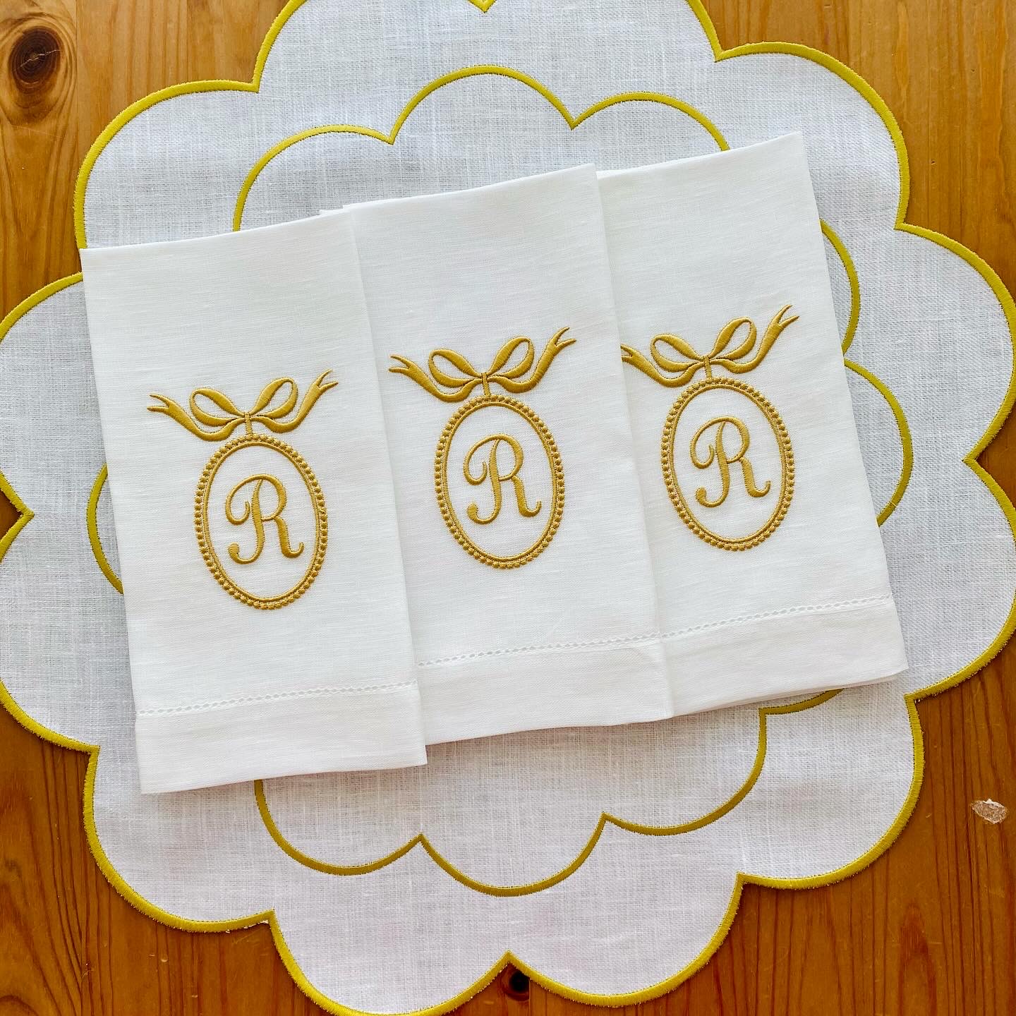 Guardanapos brancos bordados com a letra R dourada sobre um sousplat branco bordado a dourado