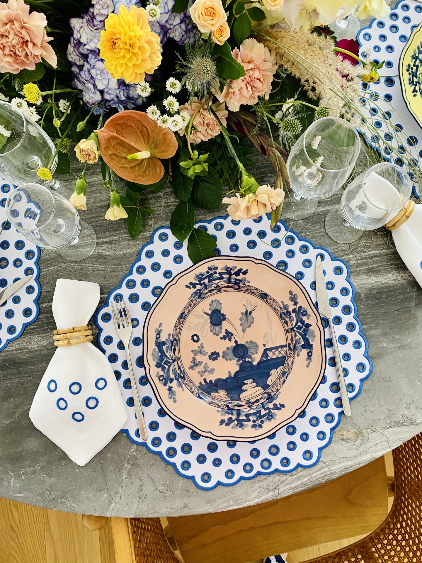 mesa decorada com prato cerâmico azul e branco, guardanapo branco, copos de vidro e arranjo floral colorido