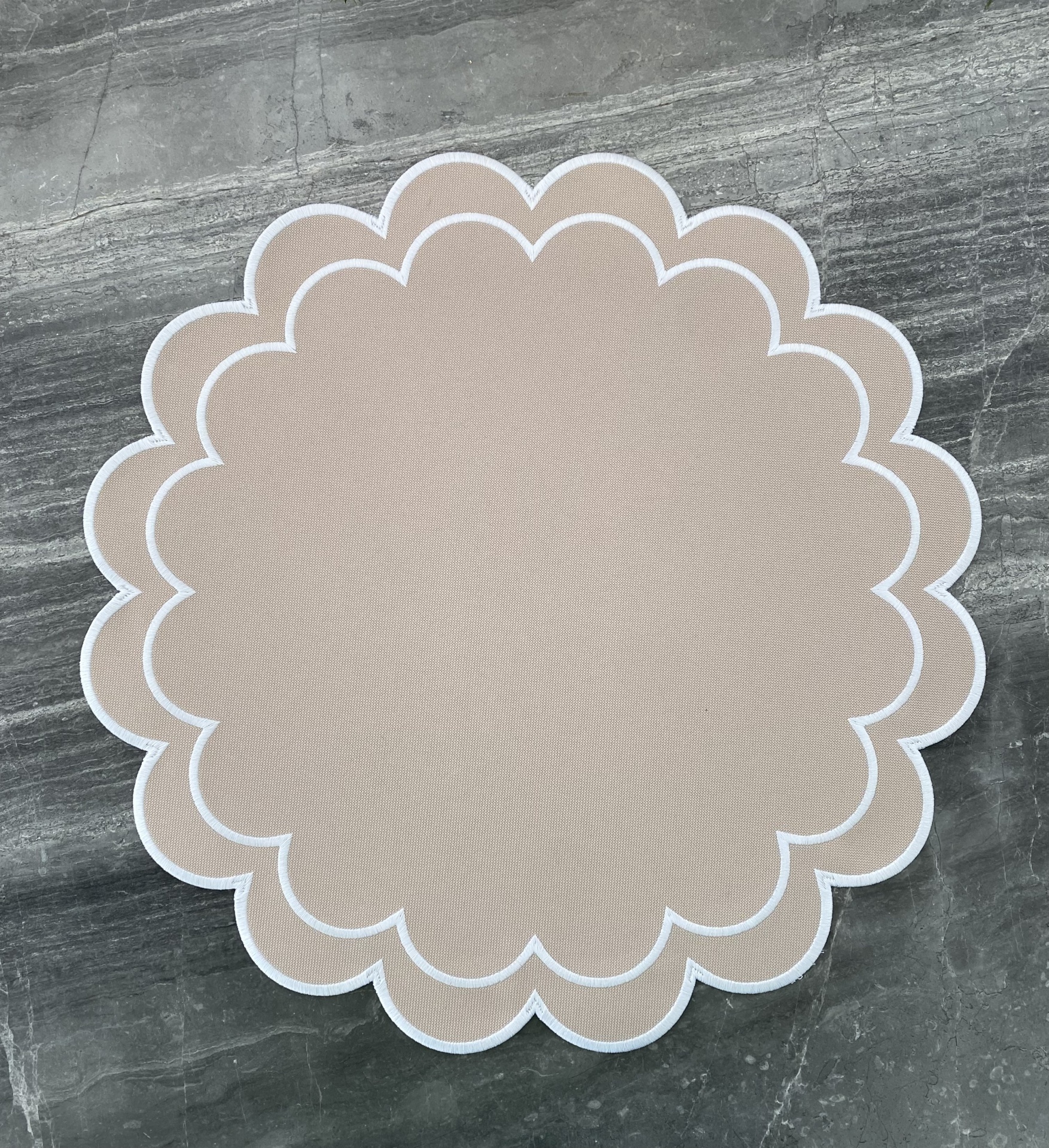 Tapete redondo bege claro com contorno branco em padrão ondulado sobre chão de pedra cinzenta