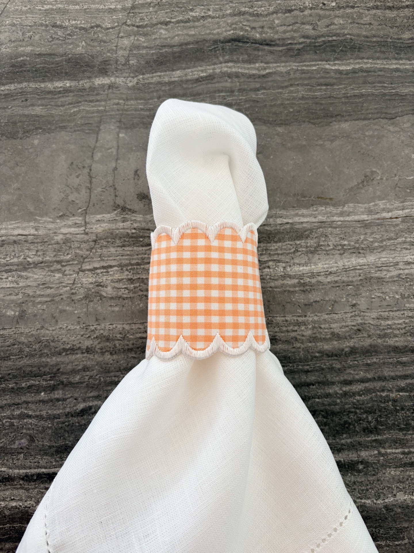 Guardanapo branco com argola laranja aos quadrados numa superfície cinzenta