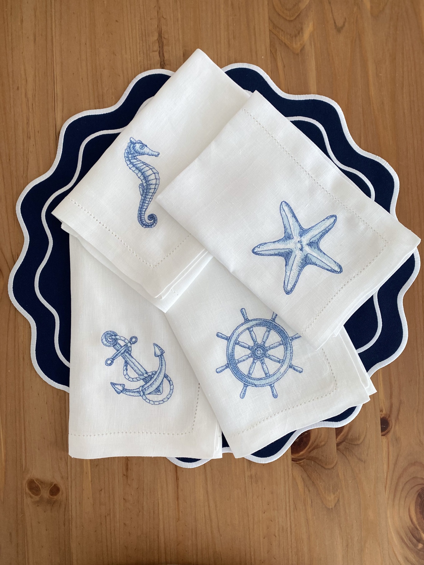 Conjunto de guardanapos brancos com bordados náuticos azuis sobre bases de mesa azul-marinho onduladas