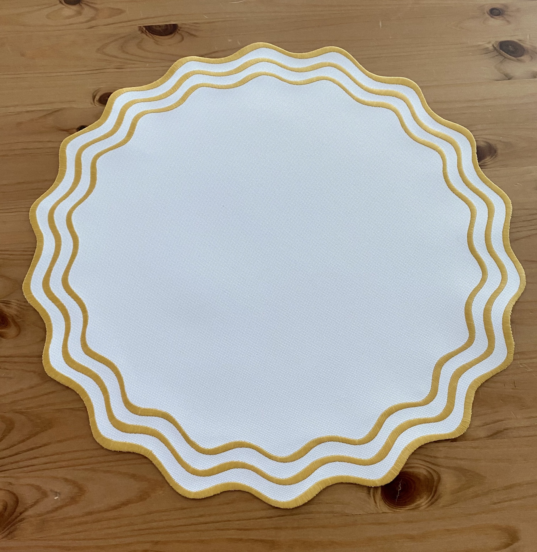 Guardanapo redondo branco com bordas douradas onduladas sobre mesa de madeira