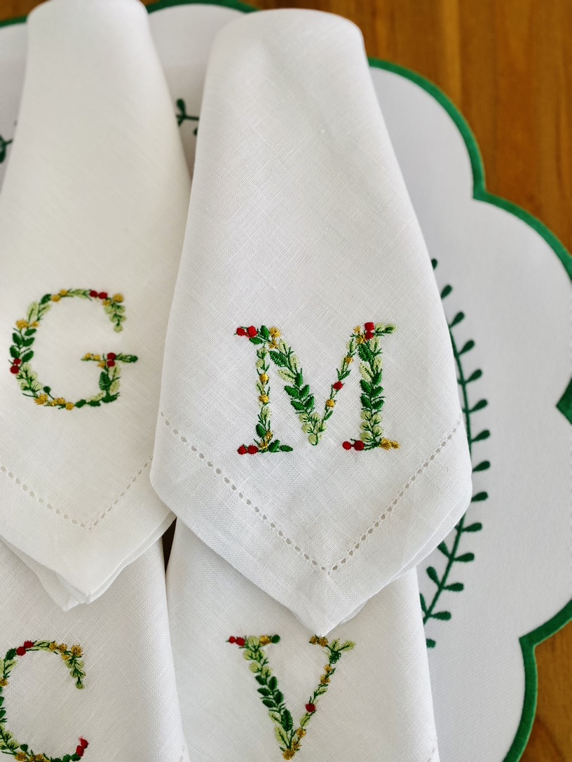 Guardanapos brancos com monogramas bordados em motivos florais coloridos sobre suporte branco com borda verde