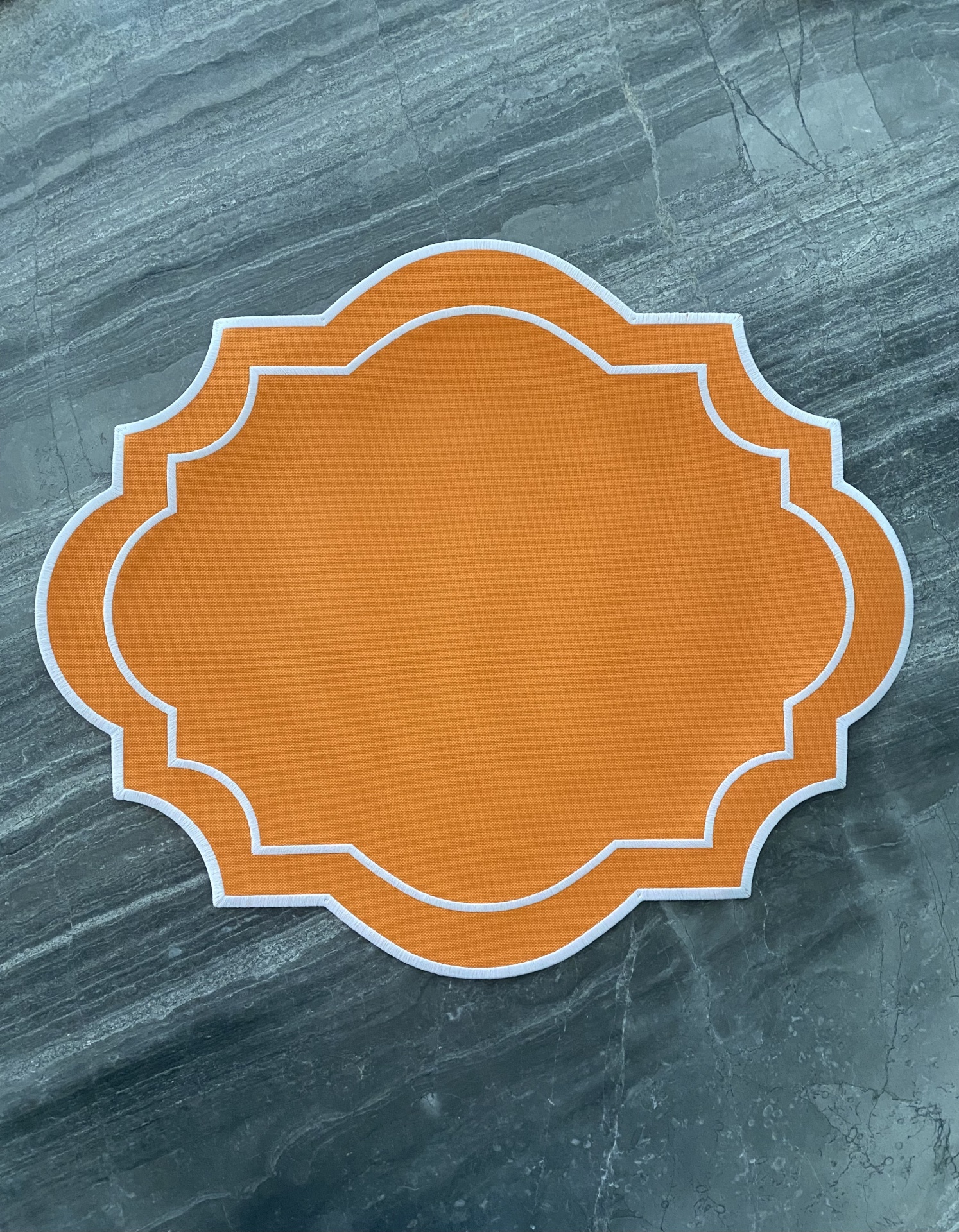 Descanso de mesa laranja com bordas brancas sobre superfície cinza tipo mármore.