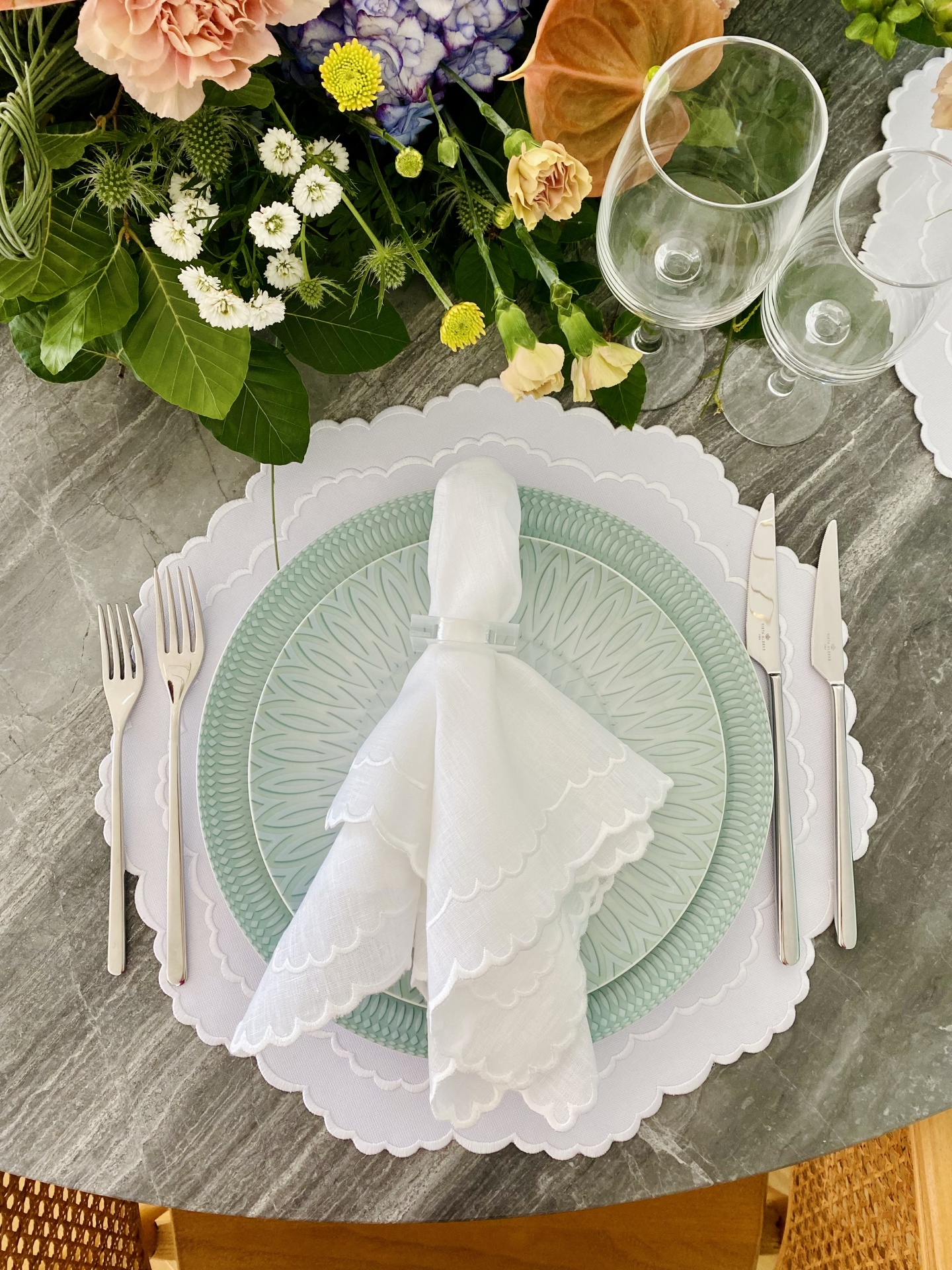 Conjunto de louça com prato verde e branco, guardanapo branco, talheres, copos e arranjo floral