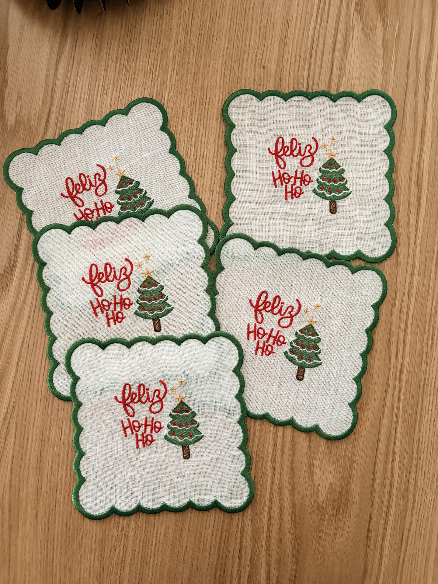 Toalhetes de tecido branco com design de Natal e borda verde sobre madeira