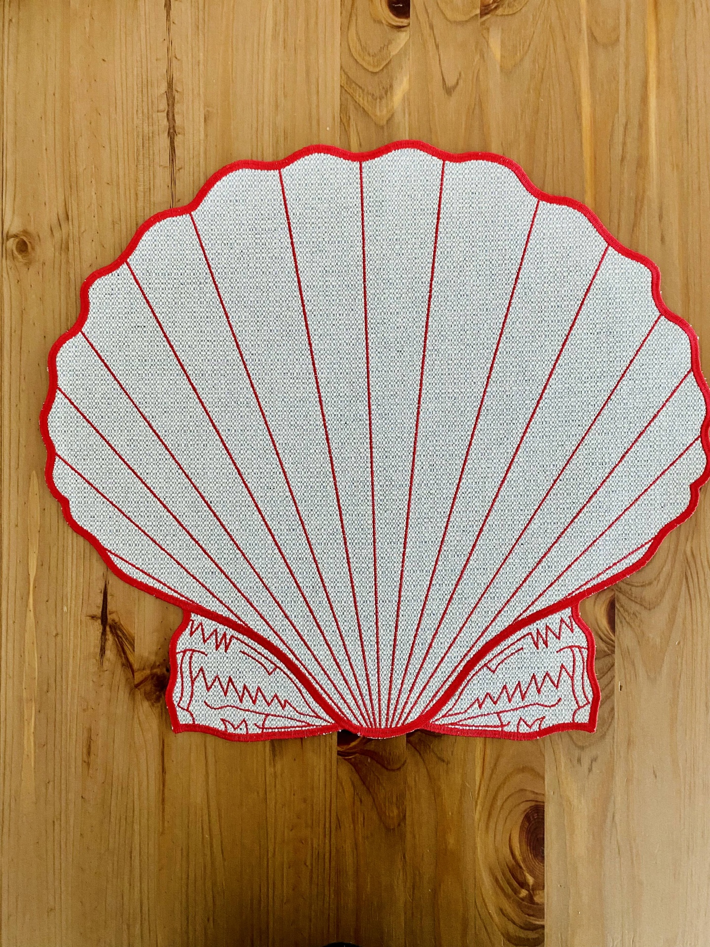 Tapete formato concha branco com linhas vermelhas sobre chão de madeira clara