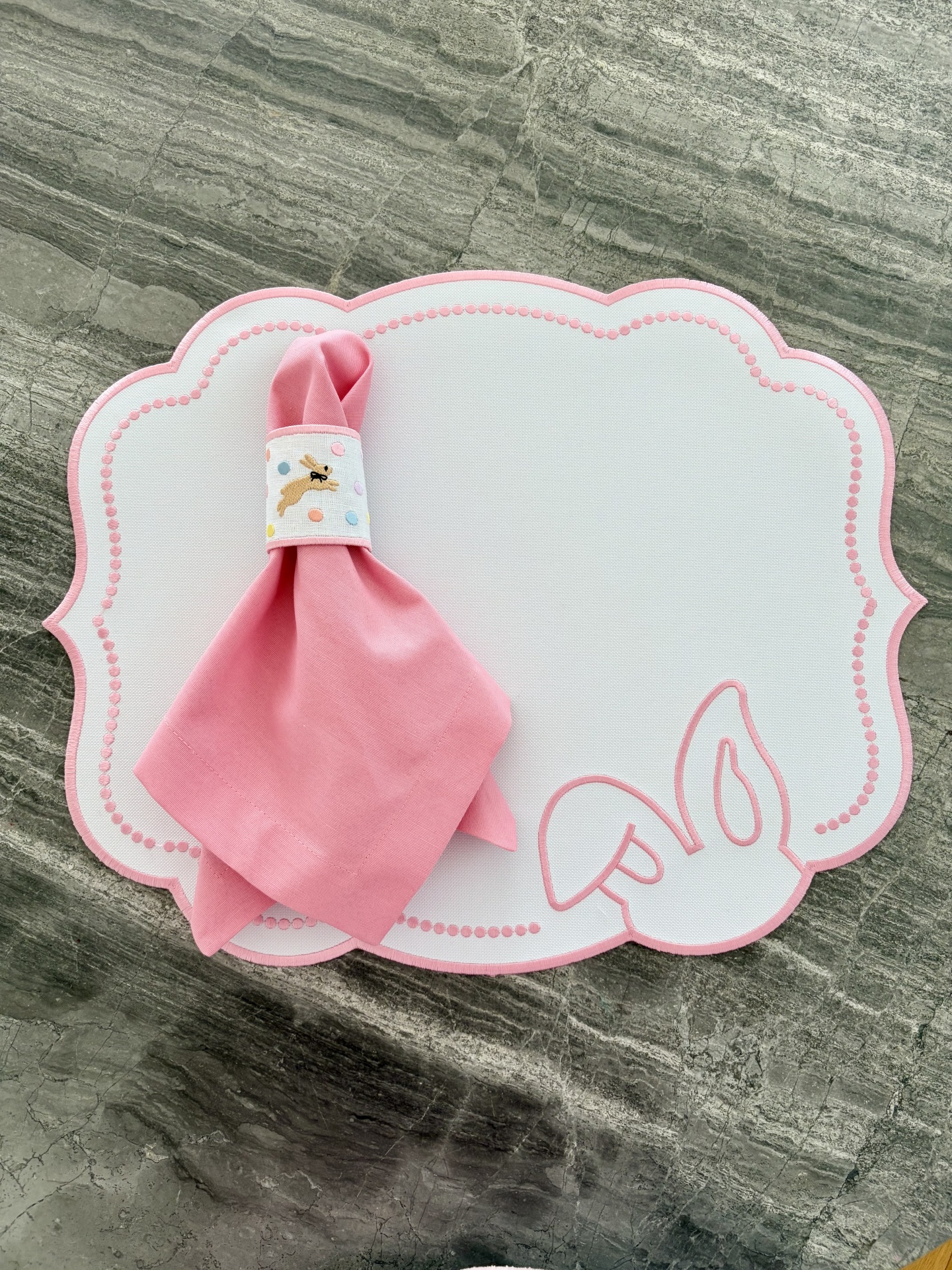 Individual branco com borda rosa e padrão, guardanapo rosa com anel decorado com coelho e pontos coloridos