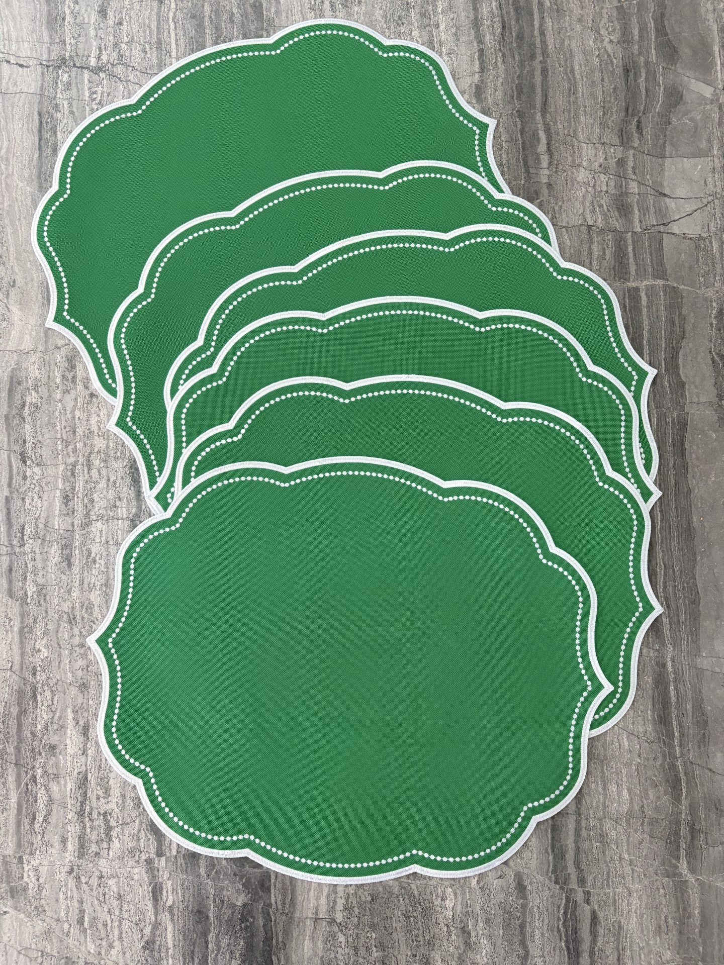 Individuais de mesa verdes com bordas brancas em tecido sobre pedra cinza